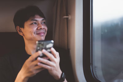 Smiling man using mobile phone by window in train