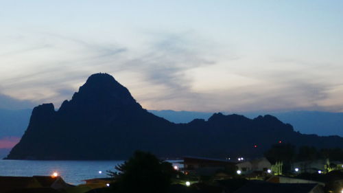 Silhouette city by sea against sky at sunset