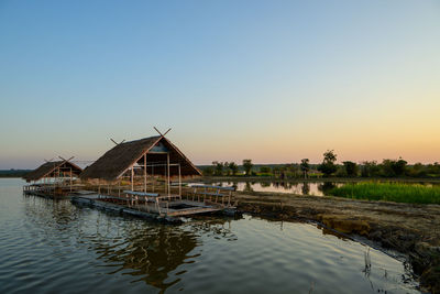 Stilt house by lake against sky during sunset