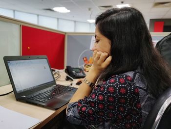 Side view of businesswoman using laptop while sitting on table at office