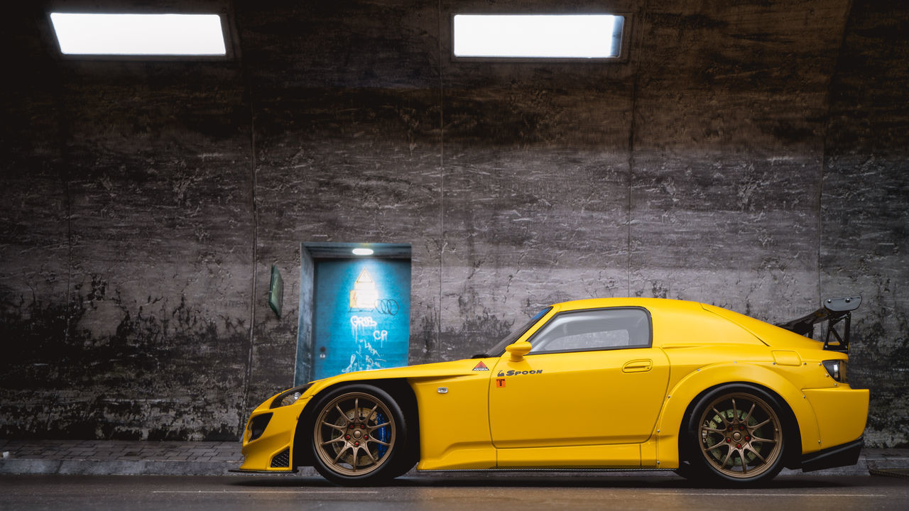 YELLOW CAR PARKED BY WALL IN ILLUMINATED STREET