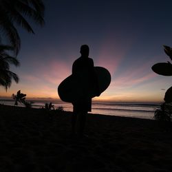 Silhouette people on beach against sky during sunset