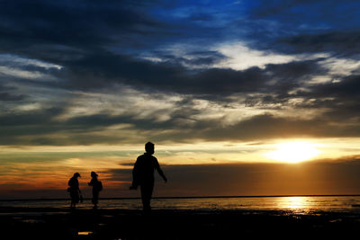 Silhouette people on beach against sky during sunset