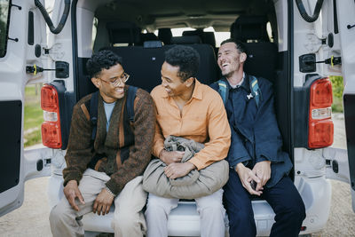 Cheerful male friends sitting in van trunk