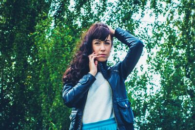 Portrait of young woman with hand in hair standing against trees