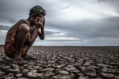 Full length of shirtless man lying on land against sky