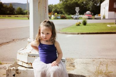 Innocent girl looking away while sitting by street on sunny day