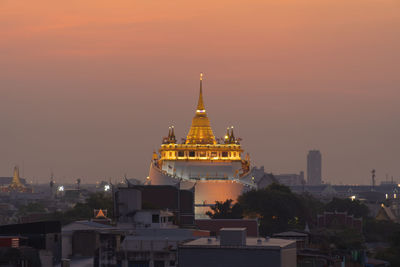 Illuminated buildings in city against sky during sunset