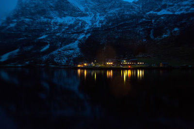 Illuminated houses by lake against mountains at night