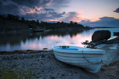 Boat moored on lake against sky during sunset