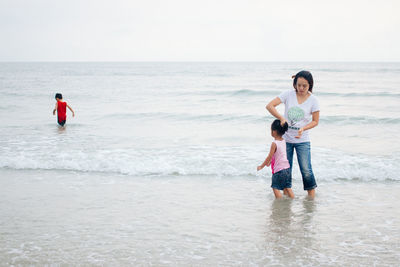 Mother with kids standing in water at beach against sky