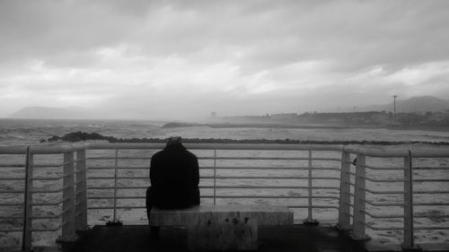 Rear view of man standing by railing against sea