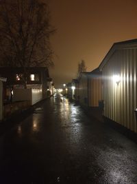 Illuminated street amidst buildings against sky at night