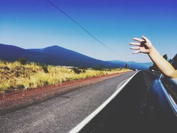 Cropped image of hand on car window at street against sky