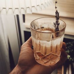 Close-up of hand holding brown clear drink with thyme