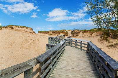 Boardwalk leading towards sand against sky