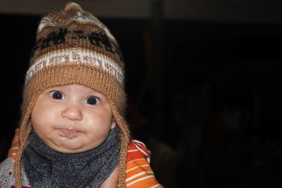 Close-up portrait of baby wearing knit hat against black background