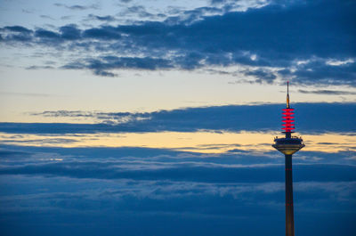 Low angle view of communications tower against cloudy sky