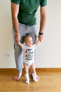 Low section of father with daughter standing by wall at home