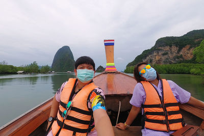 Rear view of people in boat on lake against sky