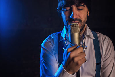 Close-up of man singing while holding microphone over black background