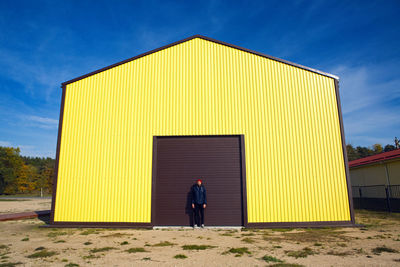 Guy in the red hat stands at the wall of the iron house in nature next to the lake