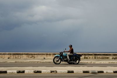 Man riding bicycle on road against sky