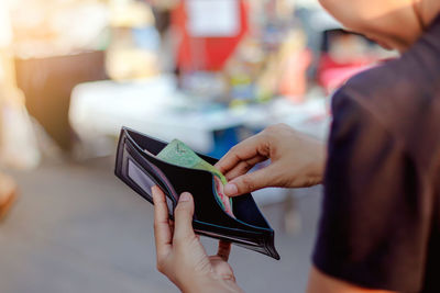 Close-up of woman holding removing money from wallet outdoors