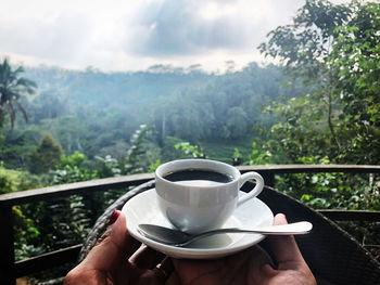 Man holding coffee cup and spoon against trees