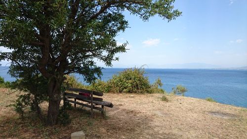 Bench in park by sea against sky