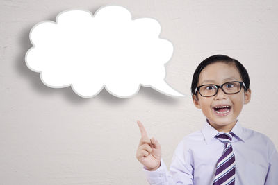 Portrait of happy boy with thought bubble standing against white background