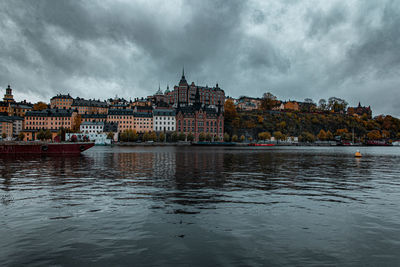 View of buildings by river against cloudy sky
