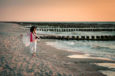 Mature woman walking on sandy beach during sunset