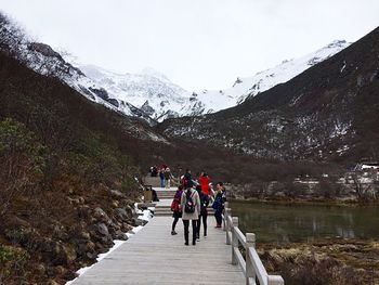 People on boardwalk by lake in valley against sky during winter