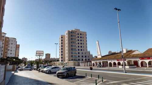 Cars on road by buildings against sky in city