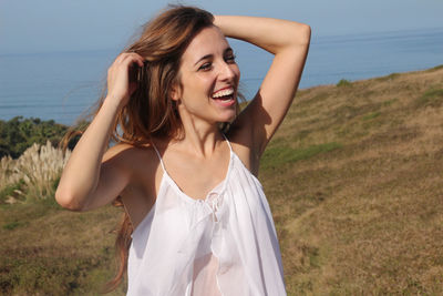 Portrait of a happy young woman smiling in a field with the sea in the background.