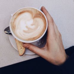 Cropped image of woman holding frothy coffee on table