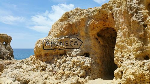 Text with arrow symbol on rock formation at shore against sky