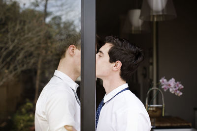 Side view of gay couple kissing while standing at doorway