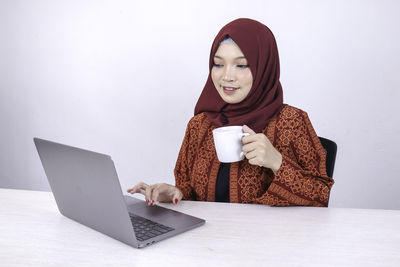 Young woman using phone while sitting on laptop