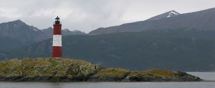 Lighthouse amidst buildings and mountains against sky