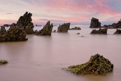 Rocks appear in the silky water of a beach in spain