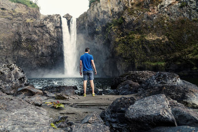 Rear view of mature man looking at waterfall while standing on rock