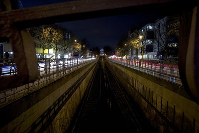 Railroad track amidst light trails on road in city at night