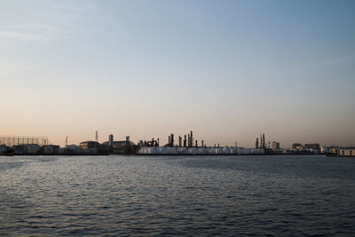 Silhouette buildings by sea against sky during sunset