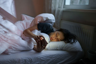 Young depressed woman in bed staring at smartphone screen, feeling envious on social media