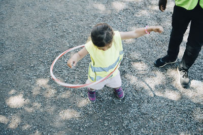 High angle view of girl playing with plastic hoop by male teacher in playground