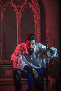 Portrait of man in costume holding sword at abandoned building during night