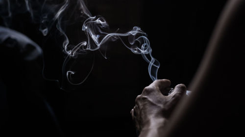 Cropped hand holding cigarette against black background