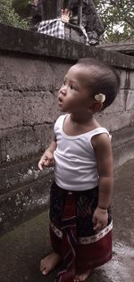 Baby girl looking away while standing against wall